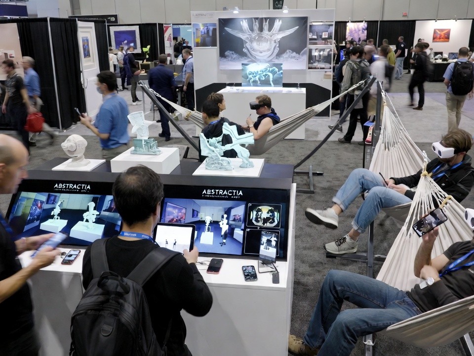 Conference attendees interacting with freestanding ABSTRACTIA machines featuring digital art displays, QR-linked collection tools, and lounge seating in an exhibition hall.